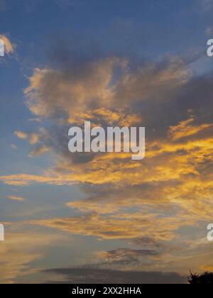 Goldene Wolken leuchten in der Abenddämmerung am Himmel und schaffen einen ruhigen Horizont mit verschiedenen Blau- und Gelbtönen, die sich nahtlos zu einer natürlichen Kunstform verschmelzen. Stockfoto