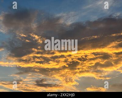 Wolken, die von den goldenen Tönen der untergehenden Sonne beleuchtet werden, erzeugen eine dramatische Farbenpracht am Himmel, während die Dämmerung in einem tiefblauen Himmel einbricht. Stockfoto