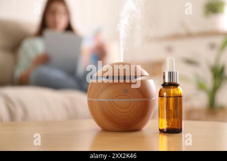 Aromadiffusor und Flasche ätherisches Öl auf dem Tisch. Frau liest Buch im Zimmer, selektiver Fokus Stockfoto