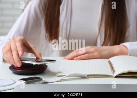 Frau, die modernes Handy auf das kabellose Ladegerät auf dem Tisch legt, Nahaufnahme Stockfoto
