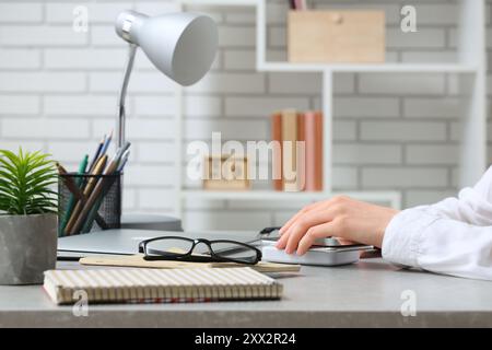 Frau mit Mobiltelefon, kabellosem Ladegerät, Laptop und Notebooks am Tisch im Büro Stockfoto