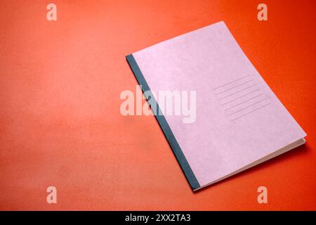 Ein rosafarbenes Notizbuch mit schwarzem Rücken sitzt auf einer roten Oberfläche. Das Notizbuch ist auf einer leeren Seite geöffnet und kann mit Ideen und Gedanken gefüllt werden. Die rote Ba Stockfoto