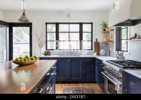 Küche mit blauen Schränken und Arbeitsflächen aus weißem Marmor mit Blick auf Waschbecken und Fenster Stockfoto