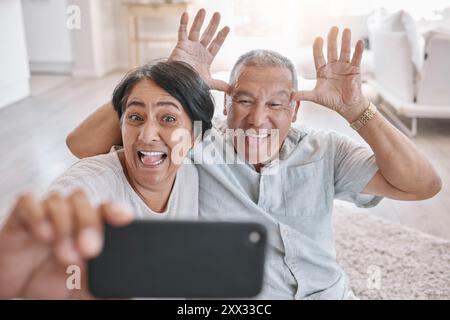 Seniorenpaar, Selfie und verrückt zu Hause für Liebe, Spaß und Entspannung im Ruhestand. Lustige, ältere Menschen und Comic-Gesicht im Wohnzimmer zum Fotografieren Stockfoto