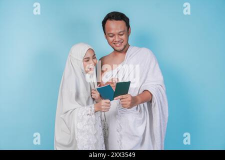 Junges asiatisches muslimisches Paar im Ihram und Gebet-Kleid, das sich gegenseitig im Pass ansieht, isoliert durch blauen Hintergrund. Hajj-Konzept. Stockfoto