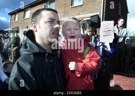 Aktenfoto vom 09/01 eines schreienden jungen katholischen Kindes in Beig, das an die Primary School des Heiligen Kreuzes im republikanischen Ardoyne District in Belfast, Nordirland, getragen wurde. 2001 gab es in Stormont Befürchtungen, dass der eskalierende Heilig-Kreuz-Konflikt dazu führen könnte, dass andere Schulen als Vergeltungsmaßnahmen blockiert werden, wie neu deklassifizierte Akten offenbaren. Ausgabedatum: Donnerstag, 22. August 2024. Stockfoto