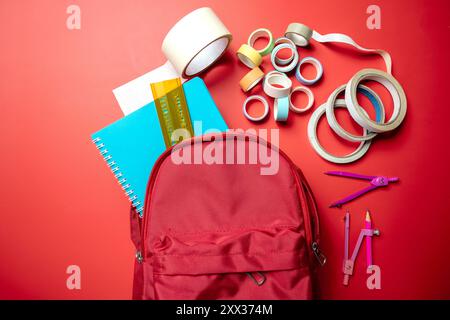 Ein roter Rucksack mit blauem Notizbuch und gelbem Lineal. Der Rucksack ist voll mit Schulmaterial Stockfoto