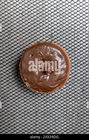 Ein Schokoladen-Mini-Donut sitzt auf einem Metallgitter. Der Mini-Donut ist mit Schokolade bedeckt und er wird frisch zubereitet Stockfoto