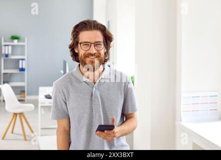 Gutaussehender Mann, der mit Smartphone in die Kamera lächelt Stockfoto