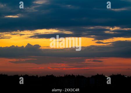 Bewölkter Himmel über den Dächern der Stadt. Die Sonne, versteckt hinter den Silhouetten der Gebäude, färbt den Himmel wunderschön Stockfoto
