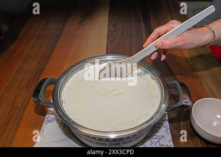 Die Frau nimmt Joghurt aus dem Topf mit einem Holzlöffel. Stockfoto