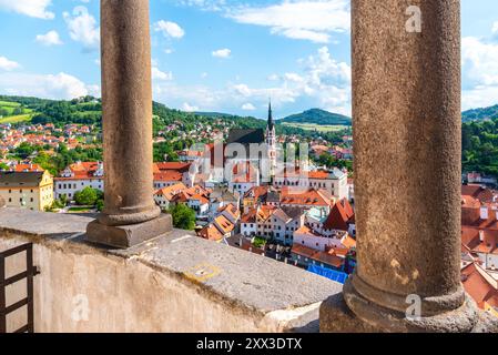 Vom Burgturm aus bietet sich ein atemberaubendes Panorama, das farbenfrohe Dächer, einen weit entfernten Kirchturm und üppige grüne Hügel unter einem hellen Himmel in Cesky Krumlov bietet, die die malerische Schönheit der Stadt veranschaulichen. Stockfoto