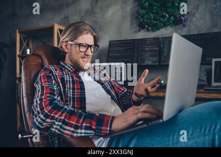 Foto von jungen blonden bärtigen Kerl IT Support Spezialist tragen kariertes Hemd sitzender Sessel verwirrt Blick auf die Insektenwebseite im Büro Stockfoto