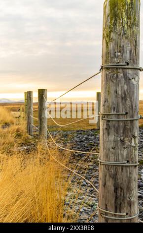 Ein Holzpfosten mit einem Seil ist auf einem Feld. Der Pfosten ist von einem Zaun umgeben und der Himmel ist bewölkt Stockfoto