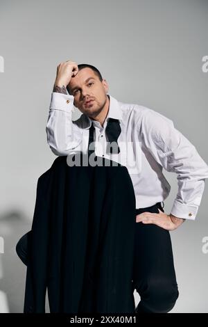 Mann in weißem Hemd und Fliege, sitzt mit schwarzer Jacke. Stockfoto