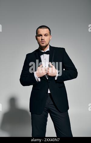 Ein Mann in einem schwarzen Smoking passt seine Fliege selbstbewusst und stilvoll an. Stockfoto