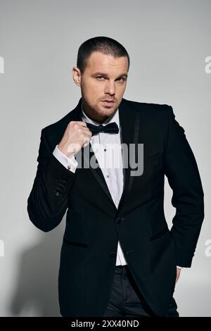 Ein Mann in einem schwarzen Smoking passt seine Bowtie an und strahlt Selbstvertrauen und Stil aus. Stockfoto