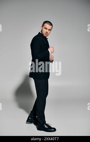 Ein düster gekleideter Mann passt seinen Manschettenknopf in einem Studio-Setting an. Stockfoto