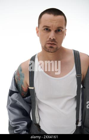 Mann in Hosenträgern, weißes Tanktop, sieht die Kamera vor weißem Hintergrund. Stockfoto