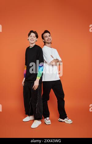 Zwei junge Freunde in stylischer Kleidung posieren vor einem orangefarbenen Hintergrund. Stockfoto