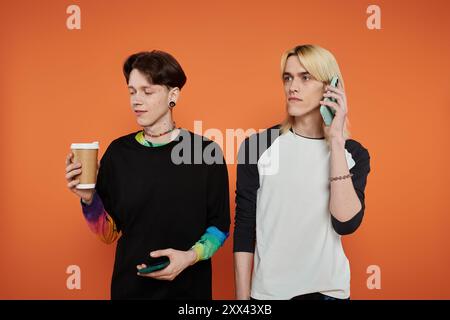 Zwei junge queere Freunde posieren in lebendiger Kleidung vor orangefarbenem Hintergrund. Stockfoto
