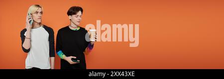 Zwei junge Freunde in stylischer Kleidung posieren vor einem orangefarbenen Hintergrund. Stockfoto