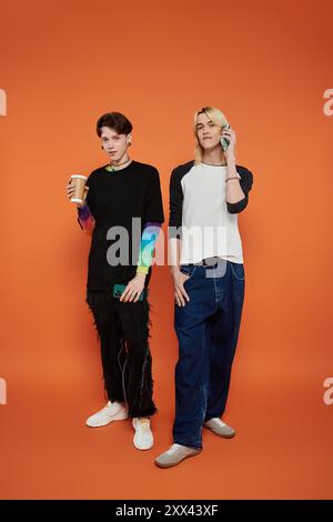 Zwei junge Freunde in bunten Outfits posieren vor einem orangen Hintergrund. Stockfoto