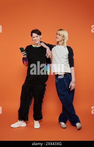 Zwei junge Freunde in stylischer, lebendiger Kleidung posieren zusammen vor einem leuchtend orangefarbenen Hintergrund. Stockfoto