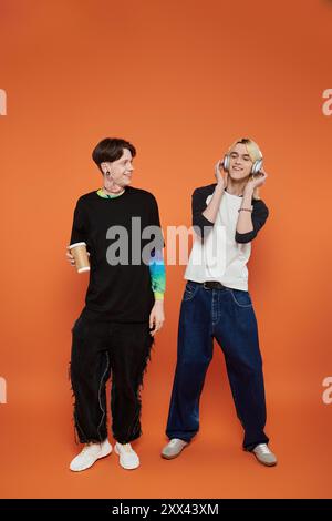 Zwei junge Freunde in stilvoller und farbenfroher Kleidung stehen auf einem orangefarbenen Hintergrund. Stockfoto