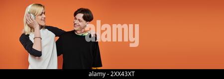 Zwei junge queere Leute in lebendiger Kleidung posieren vor einem orangen Hintergrund. Stockfoto