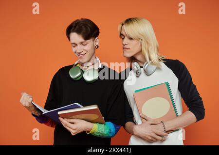 Zwei junge queere Freunde in bunten Outfits studieren zusammen vor einem orangen Hintergrund. Stockfoto