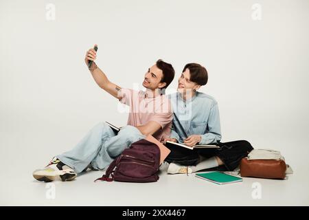 Zwei junge Studenten sitzen auf grauem Hintergrund und machen ein Selfie. Stockfoto