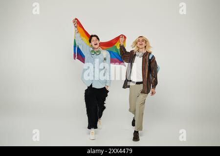 Zwei junge Leute, die eine Stolzfahne halten, in lässiger Kleidung, posieren vor grauem Hintergrund. Stockfoto