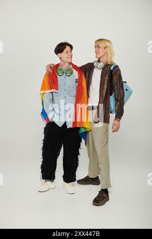 Zwei junge Schüler stehen zusammen, eine Regenbogenfahne um sie herum, in einer Geste der Freundschaft und Unterstützung für die LGBTQIA+ Community. Stockfoto