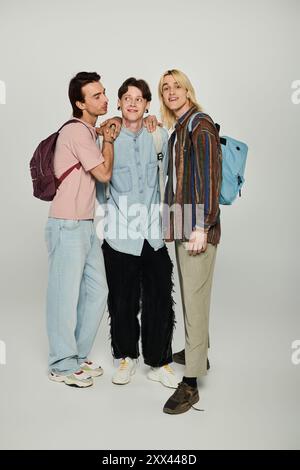 Drei junge Menschen, Mitglieder der LGBTQIA Community, stehen zusammen in lässiger Kleidung vor grauem Hintergrund. Stockfoto