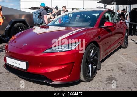 British Motor Show 2024, in Farnborough, Hampshire, England, Vereinigtes Königreich vom 15. bis 18. August 2024. Tag 2 der jährlichen Veranstaltung im Farnborough International Exhibition Centre. Ein rotes Tesla Model 3 Elektroauto auf dem Display. Stockfoto