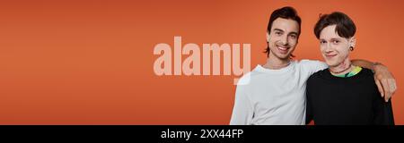 Zwei junge Freunde in lebendiger Kleidung posieren zusammen vor orangenem Hintergrund. Stockfoto