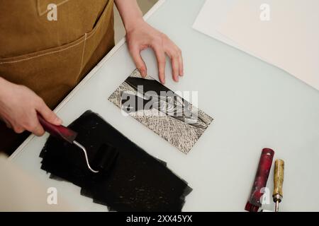 Hoher Handwinkel junger, nicht erkennbarer Handwerker, die am Schreibtisch stehen und während der Arbeit einen Paintroller über Tintenflecken halten Stockfoto