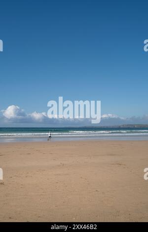 Eine Fernansicht einer Person, die allein bei Ebbe am GT Great Western Beach in Newquay in Cornwall im Vereinigten Königreich entlang der Küste läuft. Stockfoto