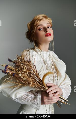 Eine junge Frau in einem weißen, gerafften Kleid hält einen Strauß getrockneter Blumen. Stockfoto