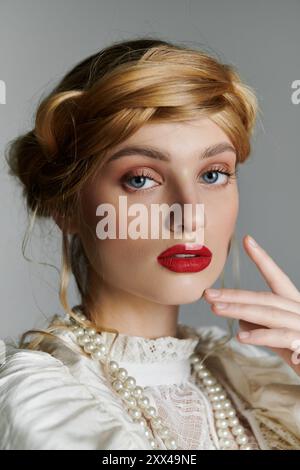 Eine junge Frau mit blondem Haar und rotem Lippenstift posiert in einem weißen Kleid mit Perlen. Stockfoto