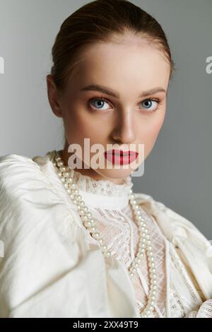 Eine junge Frau in einer weißen Spitzenbluse und einer Perlenkette blickt direkt auf den Betrachter. Stockfoto