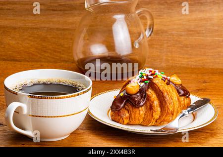 Croissant garniert mit Schokolade und Regenbogenstreuseln. Französisches Croissant garniert mit Schokolade und Regenbogenstreuseln in brauner Keramikschale mit A Stockfoto