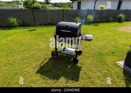 Rauch steigt von einem modernen geschlossenen Grill auf einem wunderschönen grünen Rasen. Stockfoto