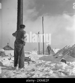 Tatsächlich 09-1949: Andenes nach dem Brand zerstörte der Brand das Telefonnetz in Andenes - das Fischerdorf verfügt über das größte Freileitungsnetz im Stadtteil Troms, das direkt durch die Feuerzone ging. Übrigens, die Telefonmitarbeiter hatten den schlimmsten Schaden repariert, als 'aktuell' zu Besuch kam - eine Arbeit, die es verdient zu erwähnen. Dies ist das dritte Mal, dass der Telefonmonteur Thomas Myrvold (im Vordergrund des Bildes) die Leitungen hier zusammengeführt und miteinander verbunden hat. Während eines Sturms im Jahr 1936 riss ein Wellblech ab und durchtrennte die Telefonleitungen, als ob sie wach wären Stockfoto