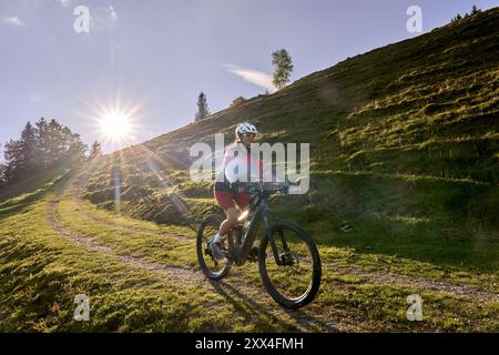Hübsche Seniorin, die ihr E-Mountainbike fährt und den spektakulären Blick über die Allgauer alpen unter der Bergkette Nagelfluh neben dem Hotel genießt Stockfoto