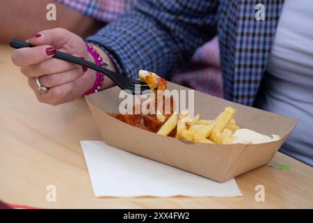 Person, die Currywurst mit Pommes frites isst, rot und weiß, allgemein, Merkmal, marginales Motiv, Symbolfoto Saskia ESKEN, SPD-Bundesvorsitzende Sarah PHILIPP, SPD-Landesvorsitzende NRW, Serdar YUEKSEL, SPD, MDL, Besuch einer Flüchtlingsunterkunft der AWO in Bochum, 21. August 2024. Stockfoto