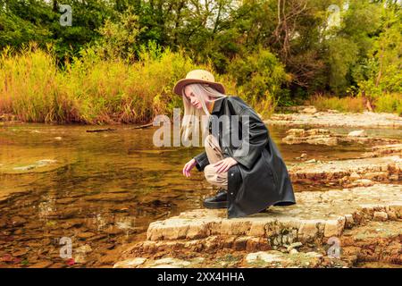 Landschaft mit einem Mädchen, das am Flussufer sitzt Stockfoto