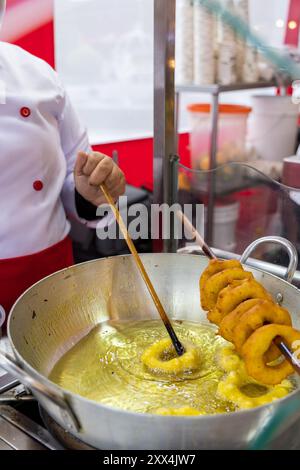 Eine Frau kocht Picarones in einer Pfanne. Das Essen wird auf einem Stock gekocht Stockfoto