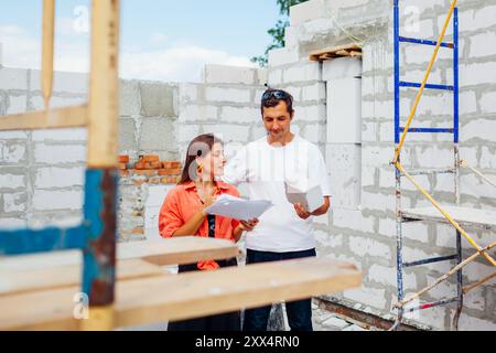 Glückliches junges Paar, das ihr zukünftiges Haus im Bau mit Gasblock überprüft. Die Familie stellt sich ihr Zuhause vor Stockfoto